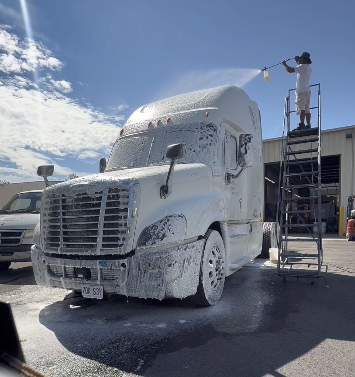 Pressure washing a white Freightliner semi truck cab at an industrial facility for deep cleaning and shine.